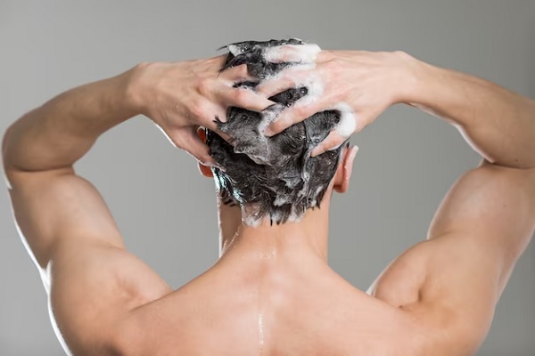 a man on his back in the shower shampooing his hair