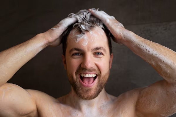 a man looking at the camera smiling while washing his hair