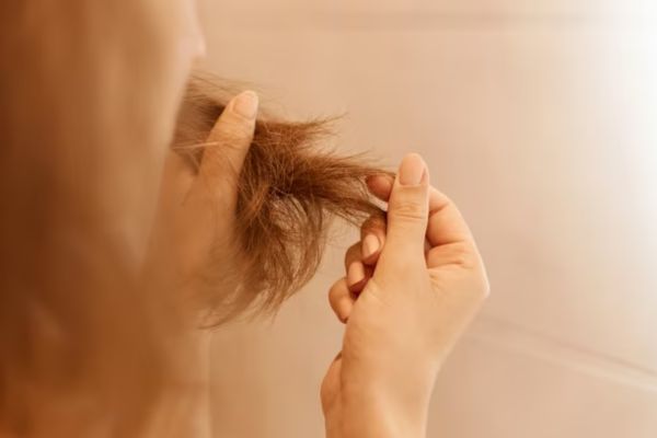 a woman looking at her hair with frizz and dry points