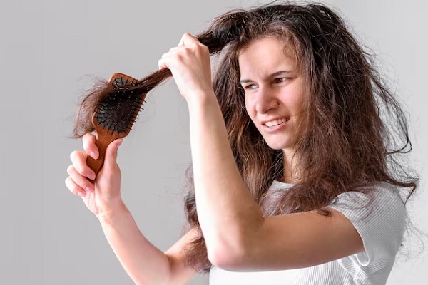 A close-up image of a woman's hand holding a red and black hair brush or comb, with strands of dark brown hair visible
