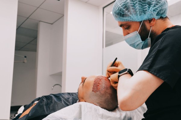 a doctor with cap performing a hair transplant surgery on a patient