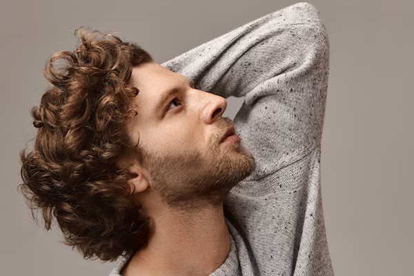 Stylish portrait of unshaven man with beautiful profile touching his curly hair